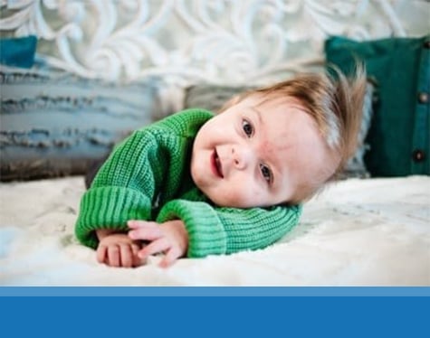 Frankie laying on a white blanket his stomach with his head tilted to the side and smiling.