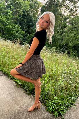 Kiki Moon posing outside and smiling. She is wearing a skirt and black top.