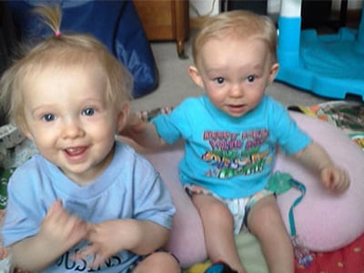 The Barker twins, McKinzie and Hudson, sitting on  a blanket on the floor and smiling.