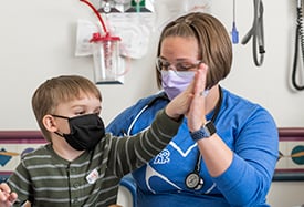 Tripp Chase giving nurse, Lindsey Fricke, a high-five at Children's Mercy. Both are wearing face masks.