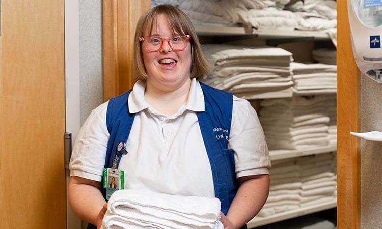 Children's Mercy volunteer with Down's syndrome smithing while holding a stack of towels at the hospital.