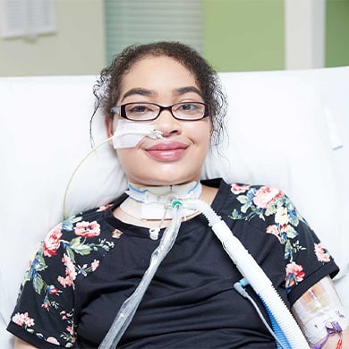 Zei Uwadia laying in a Children's Mercy bed. She is smiling while having a tube coming our of her nose and neck to help her breathe.