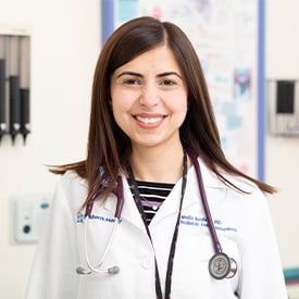 Dr. Nadia Ibrahimi smiling while wearing a white coat and stethoscope around her neck.