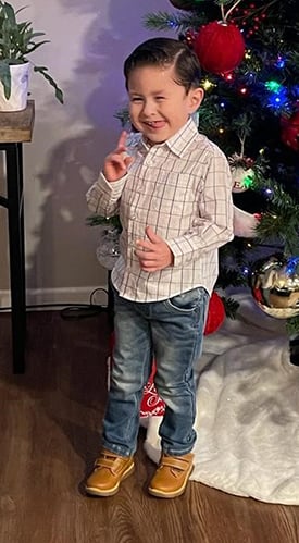 Elijah standing in front of a Christmas tree. He is winking and sticking out his tongue.