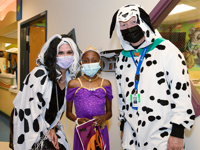 Children's Mercy CEO, Paul Kempinski, and staff member, Trista, dressed as Dalmatians, alongside a patient in a Halloween costume. 