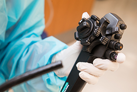 A gloved hand holding a instrument used in an upper endoscopy procedure.