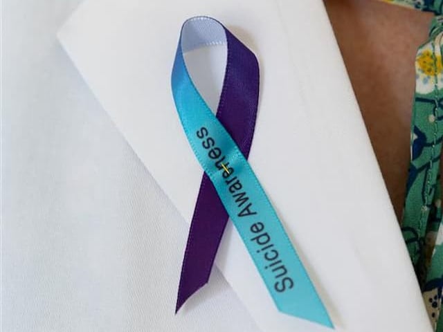 Blue and purple ribbon pinned to white shirt with words "Suicide Awareness" on the blue side of ribbon 