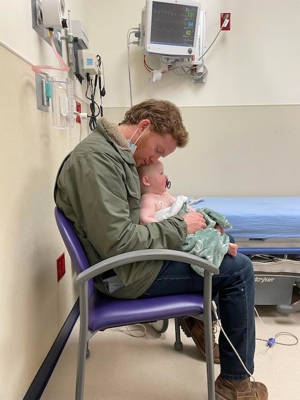 Dad holding Auggie sitting in chair inside patient room 