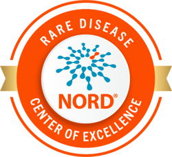 Circular badge with an orange border and gold ribbon. Inside, blue molecular-style graphic with one orange dot and the word NORD® in bold orange letters. Surrounding text reads Rare Disease Center of Excellence.