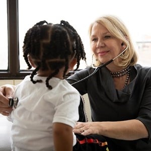 Female doctor using a stethoscope on a little girls back to listen to her lungs