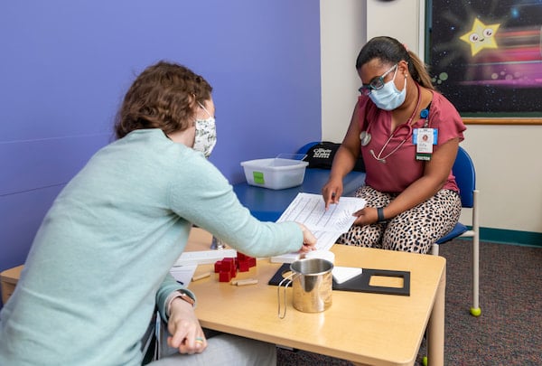 Two masked, female medical professionals look at a file together in an office setting.