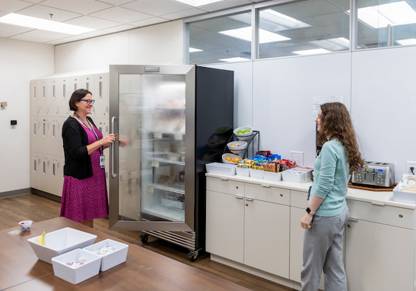 Two women chat in an office kitchen.