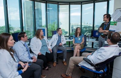 Several male and female clinicians, many in white coats, gather together in an office setting.