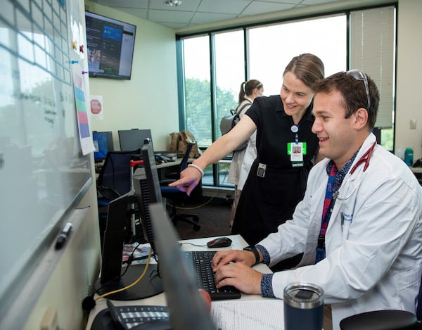 Two clinicians, one male and one female, look at a computer monitor together in an office setting.