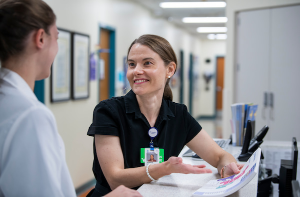 A female physician smiles and talks with another female in a hospital hallway.