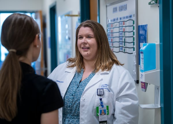 A photo of a female physician in a white coat talking with another clinician.
