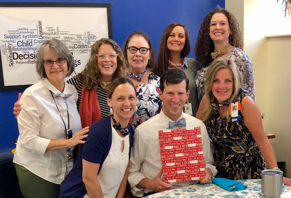 A group of people, all wearing bowties, gather around a man holding a gift.