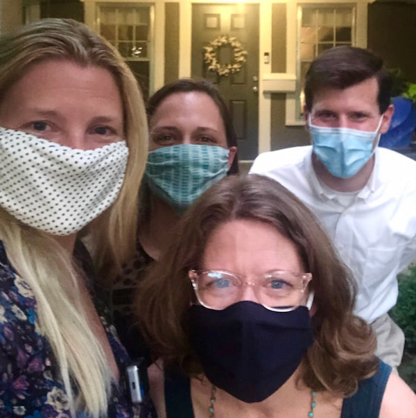 Four masked members of the Hospice Fellowship staff pose together outside a front door.