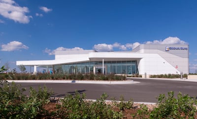 Exterior view of a modern Children’s Mercy Wichita healthcare facility with a white façade, large glass windows, landscaped greenery, and a clear blue sky with scattered clouds.