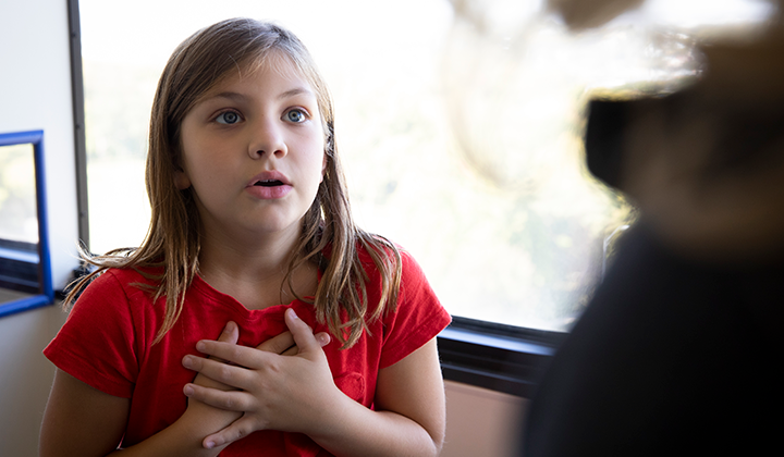 A young girl holds her hands to her chest and breathes in during an asthma doctor's appointment.