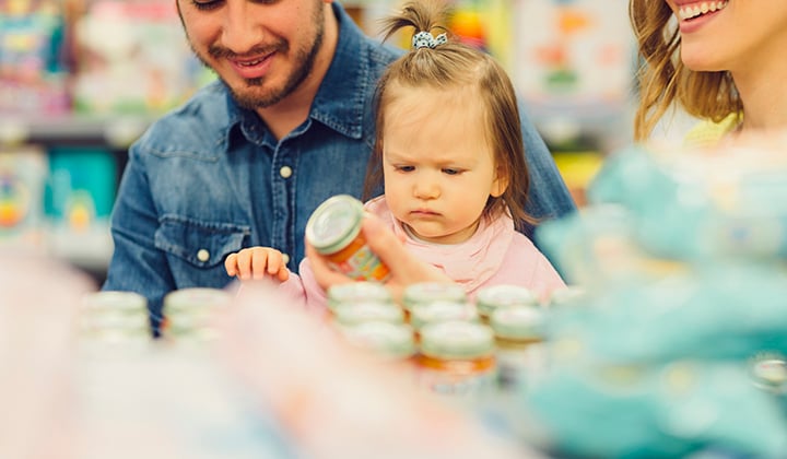 Family with young baby holding baby food jar in a grocery store.