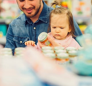 Family with young baby holding baby food jar in a grocery store.