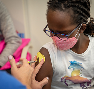 Young girls looks at arm while a nurse is giving her a vaccine and using a ShotBlocker.