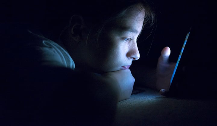 Teen girl with mobile phone screen glowing while sitting in the dark.