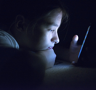 Teen girl with mobile phone screen glowing while sitting in the dark.