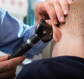 Close up of a child's back of the head while a doctor uses an otoscope to look in his ear.