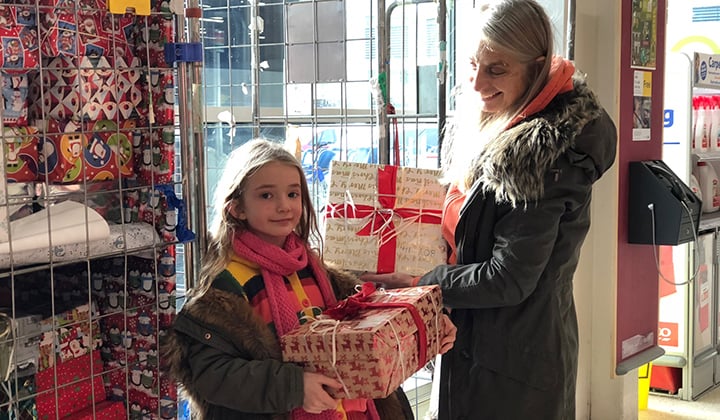Mom and young girl hold holiday gifts.
