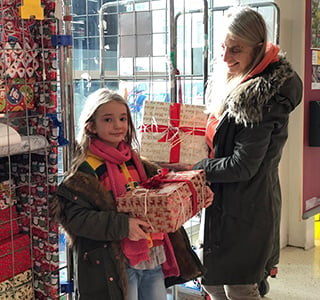 Mom and young girl hold holiday gifts.