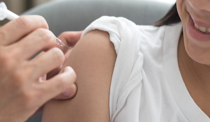 Preteen girl smiling while receiving vaccine shot. 