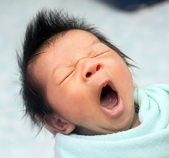 Newborn baby wrapped in a swaddle and yawning. 