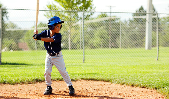 Young boy wears blue baseball uniform and holds bat over the plate while looking at the mound.