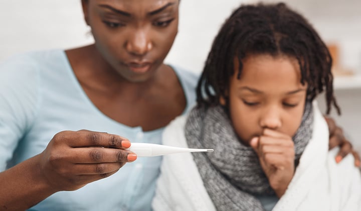 Mom looks worried as she reads a thermometer next to her coughing child.
