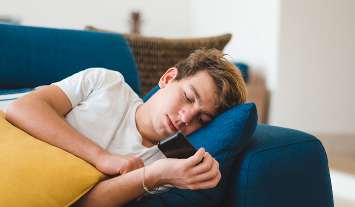 Teenage boy laying on couch with phone