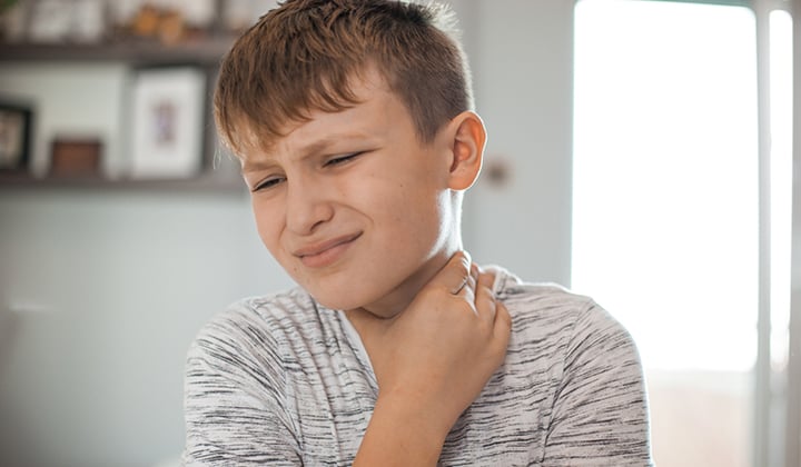 Young boy holds hand to throat and winces in pain. 