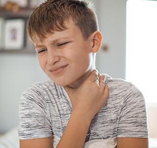 Young boy holds hand to throat and winces in pain. 
