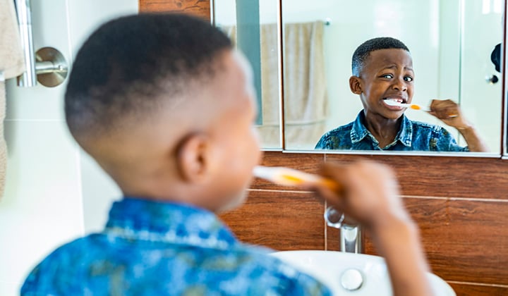 Young child looking in a mirror while brushing his teeth.