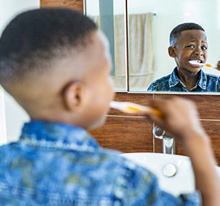 Young child looking in a mirror while brushing his teeth.