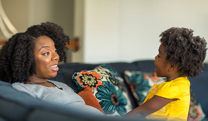 Mom sits on couch and listens to toddler talking to her. 