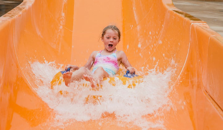 Young girl rides an inflatable tube down a waterpark slide.