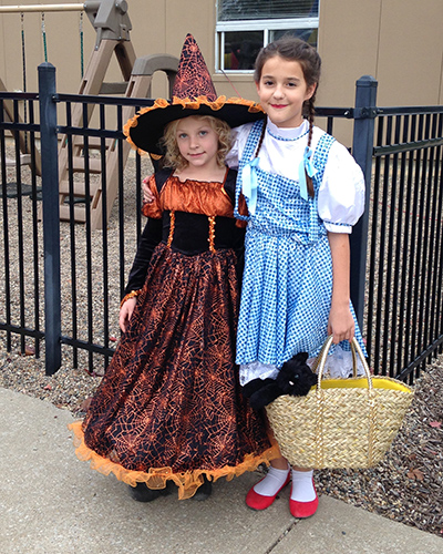Two girls hug while wearing a Dorothy and witch costume from the Wizard of Oz.