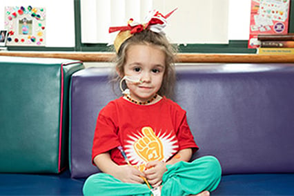 Little girl with a gold, red and white bow in her hair, and a tube running from her nose and taped to her face