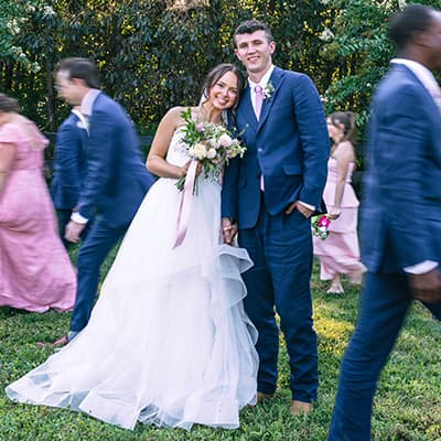 Ashleigh in a white wedding dress holding bouquet, hugging her husband in a navy blue suit pink tie 