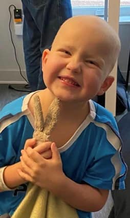 A little boy in a hospital gown smiles while holding a stuffed bunny blanket.