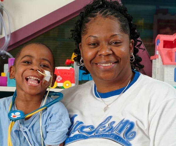 Young black male toddler poses, smiling next to his mother.
