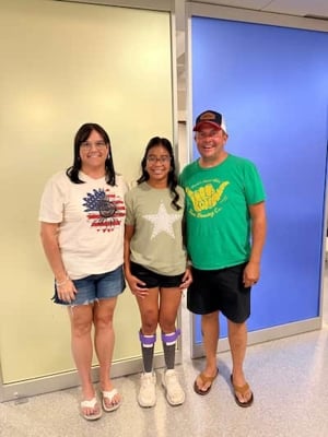 Karli and parents standing in front of blue wall.