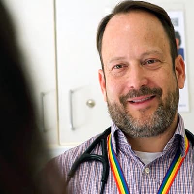 Male doctor smiles at a patient who is not seen, only the patient’s hair is showing.